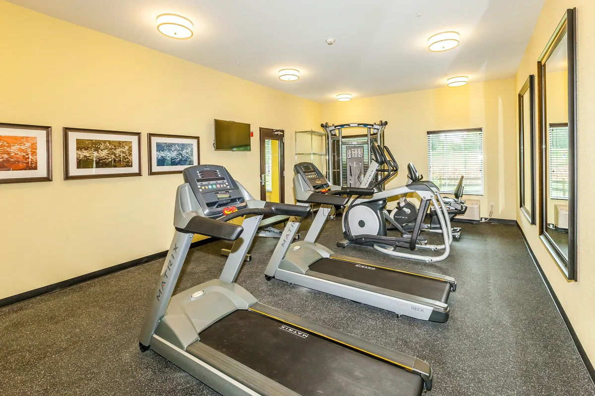 This interior image shows a well-equipped fitness center featuring treadmills, an elliptical machine, weight machines, wall art, and mirrors. The space is bright and clean, exuding a motivating atmosphere ideal for both solo workouts and group fitness sessions.