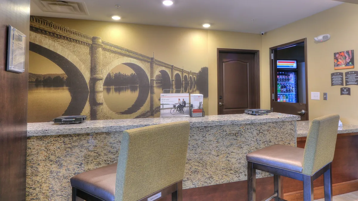 This interior image features the check-in area with a granite countertop, a mural of a bridge that hints at local scenery, a comfortable seating area, and an information display. The space feels friendly and professional, ideal for guests preparing for their day or seeking information about local attractions.