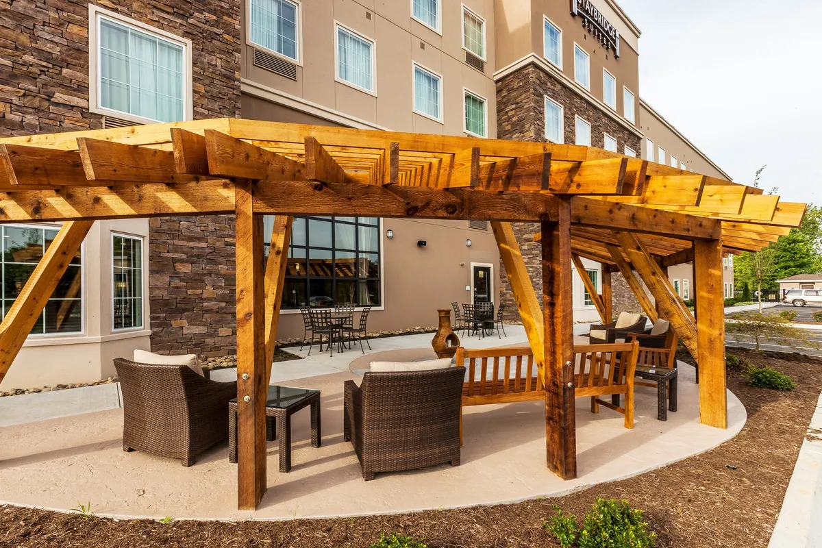 An outdoor area with a wooden pergola, comfortable seating, stone wall accents, and the hotel’s facade in the background. Guests are relaxing, socializing, and enjoying coffee in the serene outdoor space.