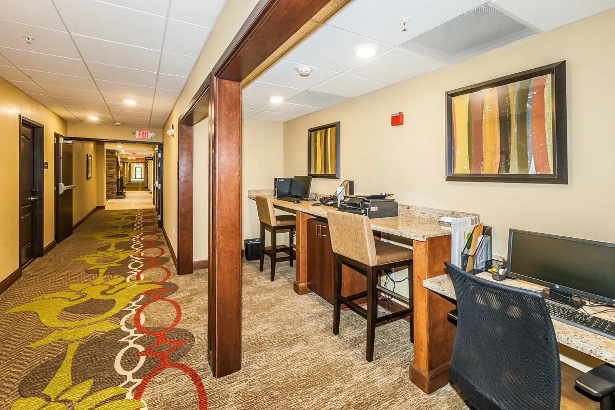 A modern, well-lit workspace featuring computers and individual workstations, accented by colorful artwork and a vibrant carpet. The atmosphere is both productive and welcoming, ideal for business travelers or digital nomads.