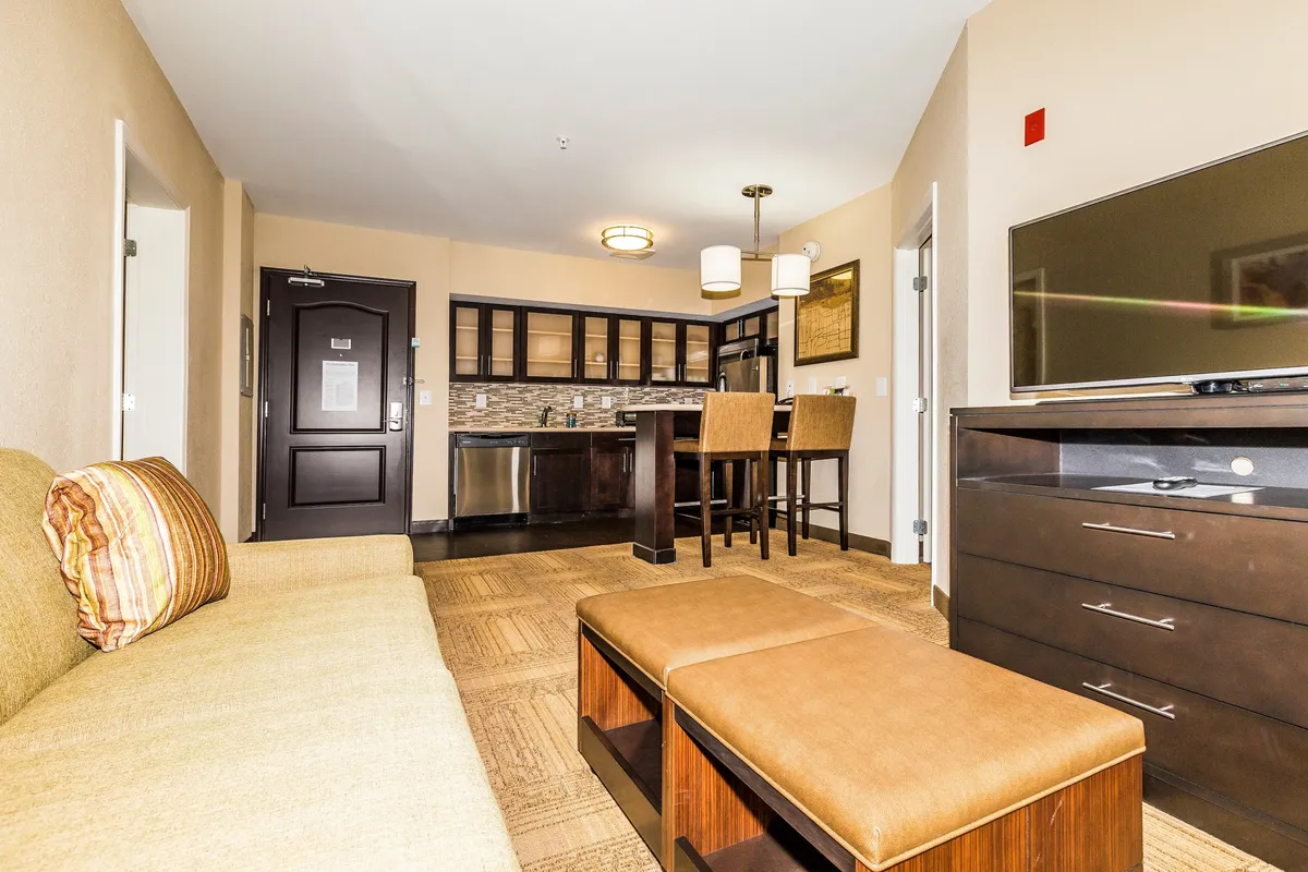A cozy, modern suite interior featuring a plush sofa, inviting dining table, wall-mounted TV, and a fully equipped kitchenette—perfect for relaxing, dining in, or enjoying a movie night after exploring Knoxville's vibrant Turkey Creek district.