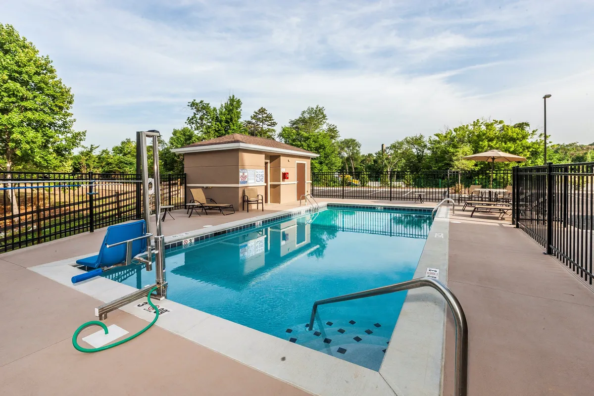 This image captures the vibrant seasonal outdoor pool area, complete with inviting blue water, poolside lounge chairs, and a cozy pool house in the background. The scene is set during daylight hours, offering a relaxed and enjoyable atmosphere for swimming, sunbathing, and socializing.